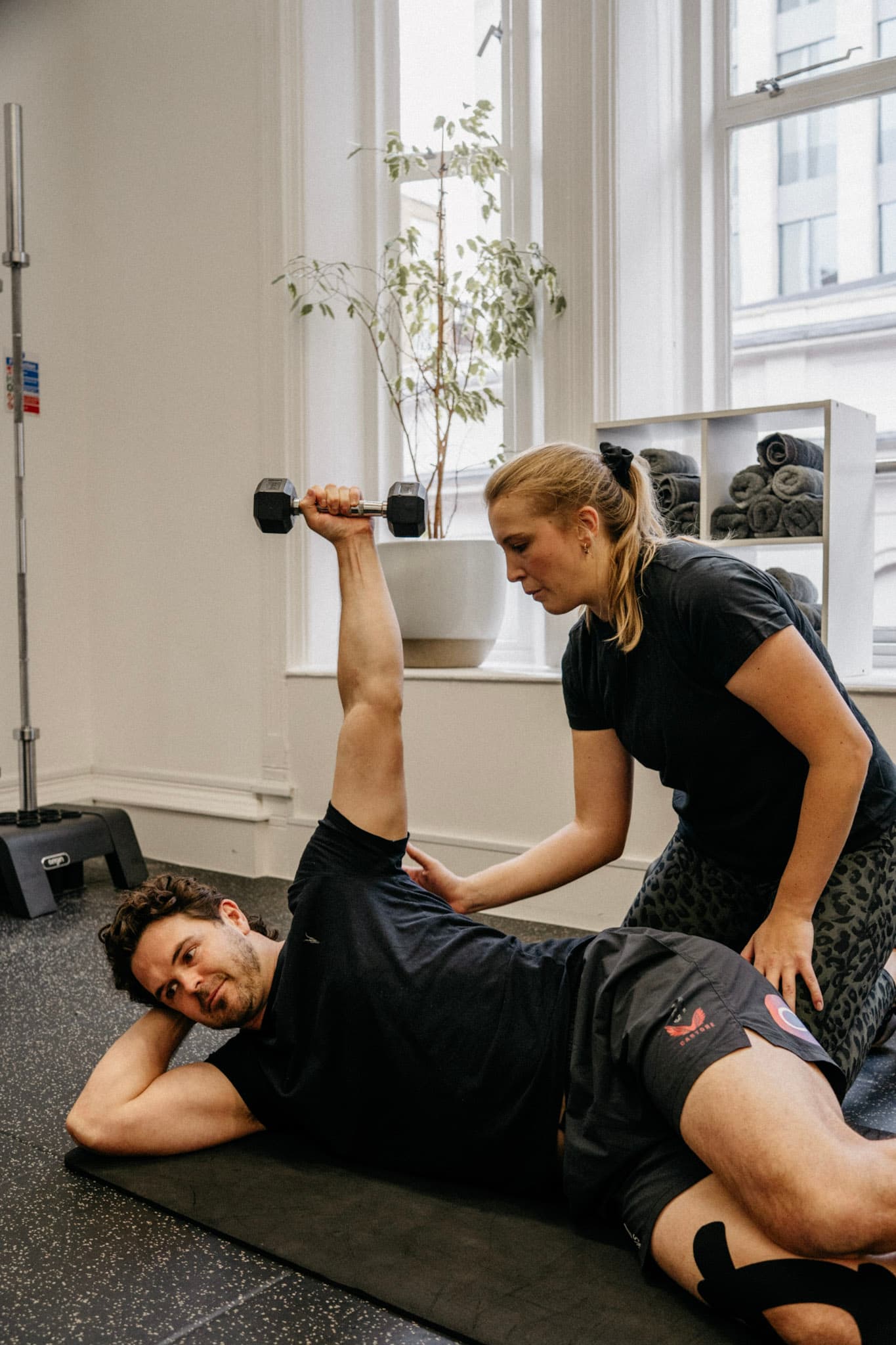 Physiotherapist guiding a client through a weighted hip and shoulder strengthening exercise