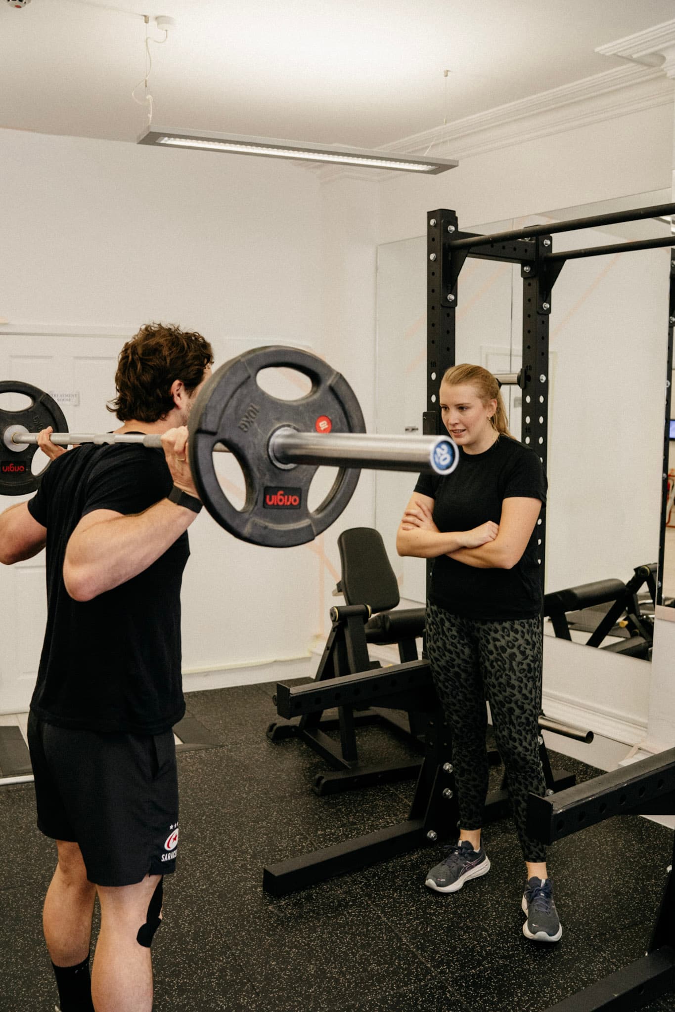 Physiotherapist supervising a client through a barbell squat in the clinic gym