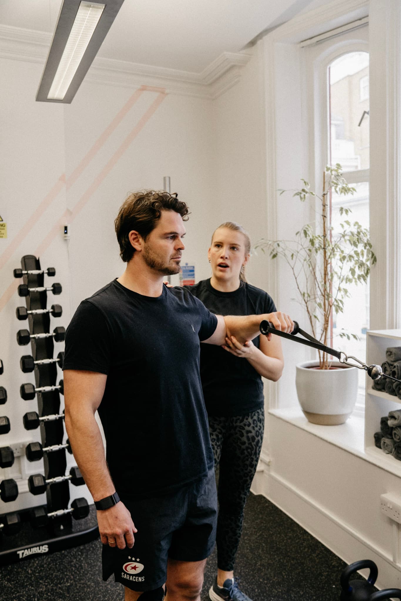 Physiotherapist guiding a client through a resisted shoulder exercise on a cable pulley